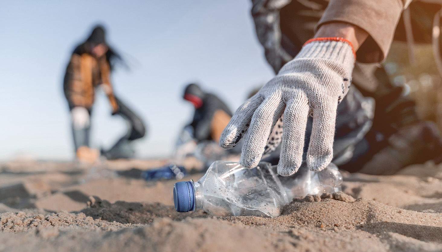 Person wearing gloves picking up a plastic bottle from the beach